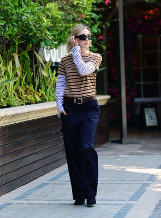 A photo of Saoirse Ronan wearing a striped Kallmeyer short-sleeve gold T-shirt with a white striped T-shirt underneath, a wide belt, and wide-leg trousers.