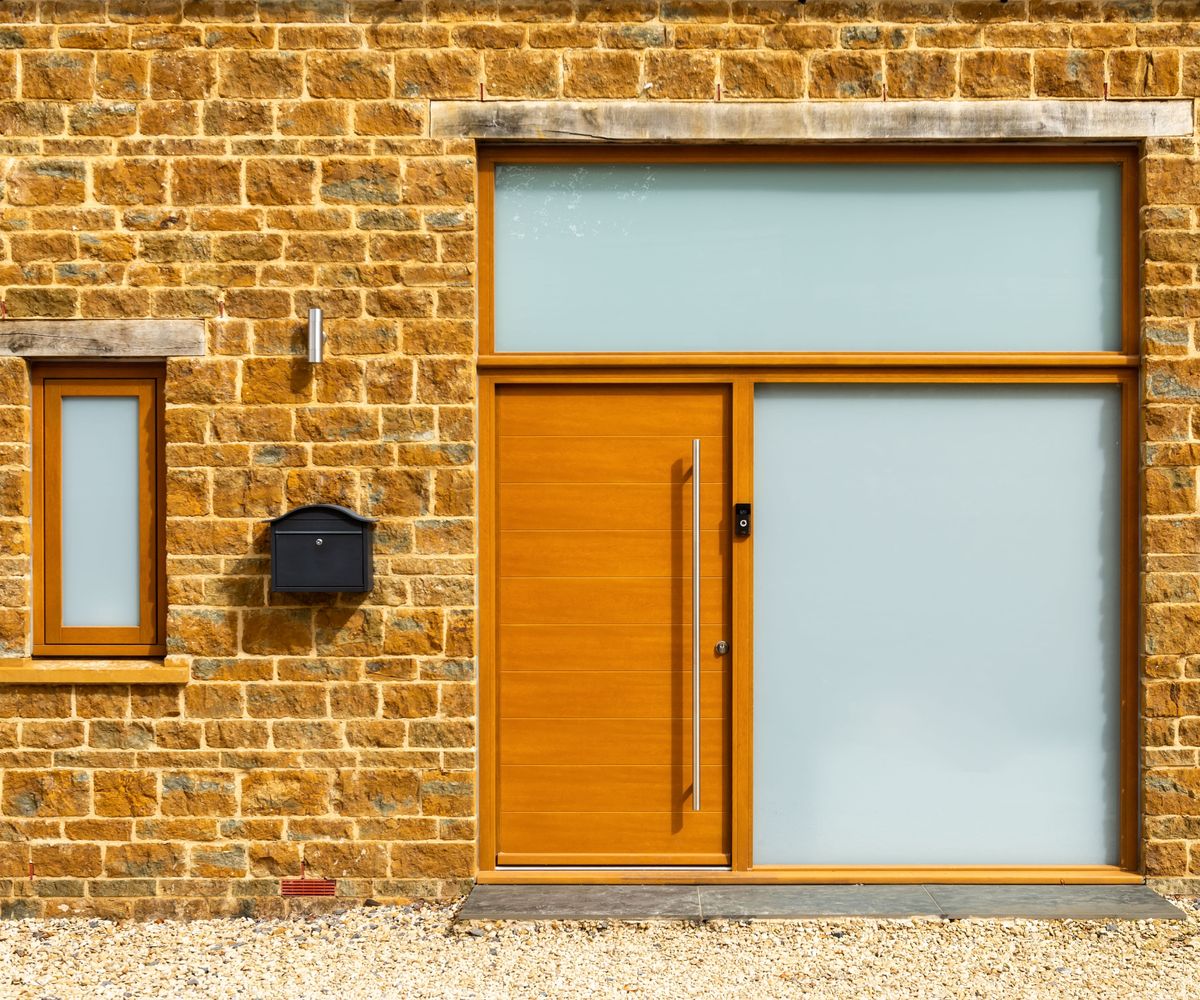 Stone-clad house with Kloeber timber FunkyFront front door featuring a long handle, next to two large panels of glazing