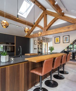 inside kitchen of oak frame extension with exposed beams and modern walnut and black kitchen units, chrome lights and leather bar stools