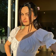Camila Mendes wears a white dress with a pink bow in her hair