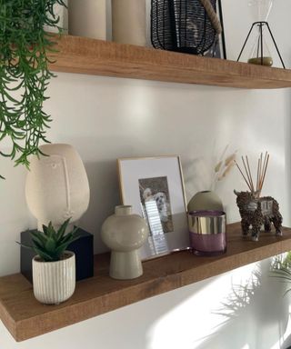 Two wooden wall shelves with candles, frames, and vases on them