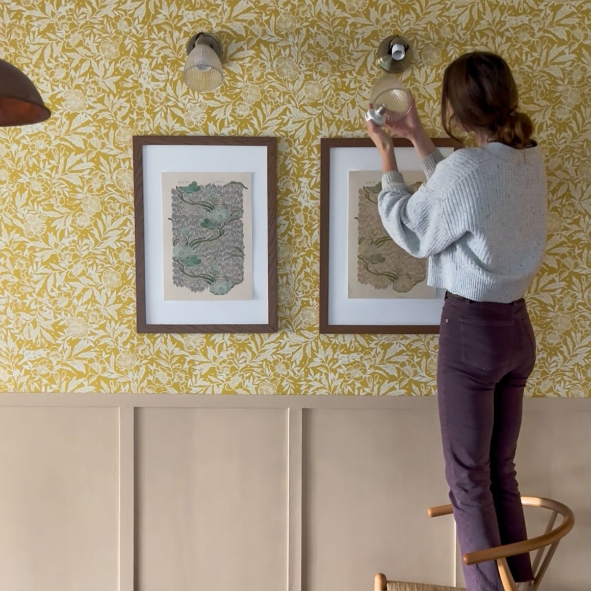 woman hanging lights above pictures on a wall