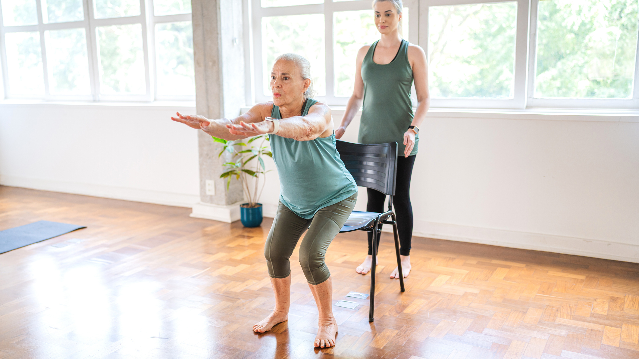 Woman squatting into chair with a personal trainer behind her