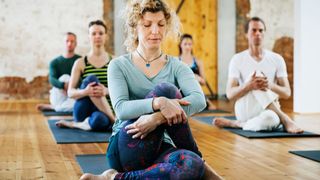 Woman sitting cross legged on a yoga mat in beginner's class with eyes closed