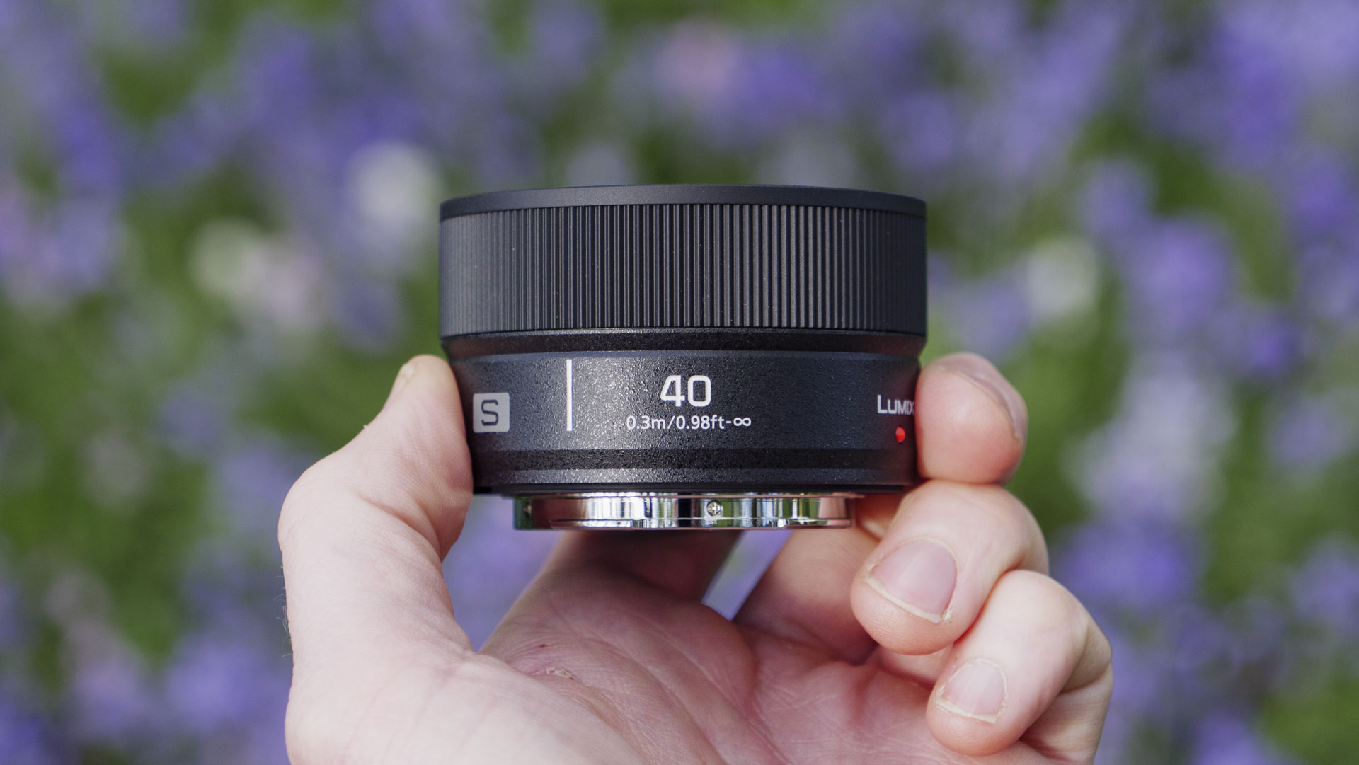 The Panasonic Lumix S 40mm F2 lens in the hand, with natural bluebell backdrop