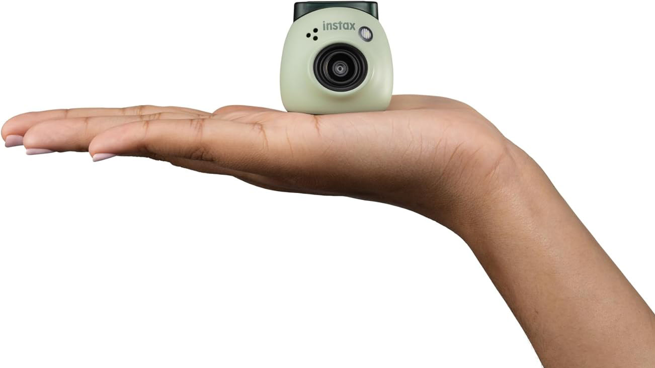 Fujifilm Instax Pal in green color on a white background and placed in the palm of a person's hand