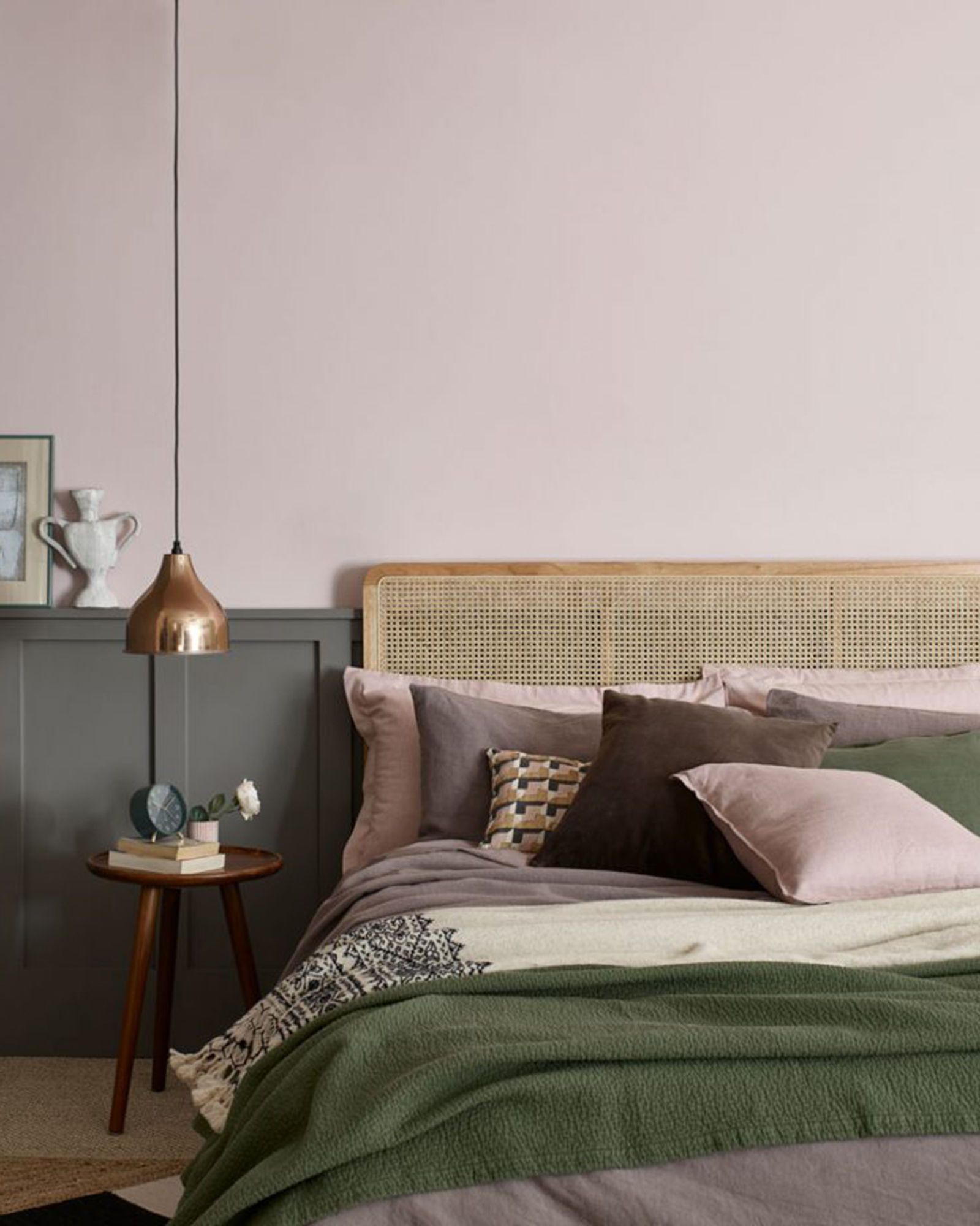 A dusky pink walled bedroom with a poorly made bed with olive and pink throws on it