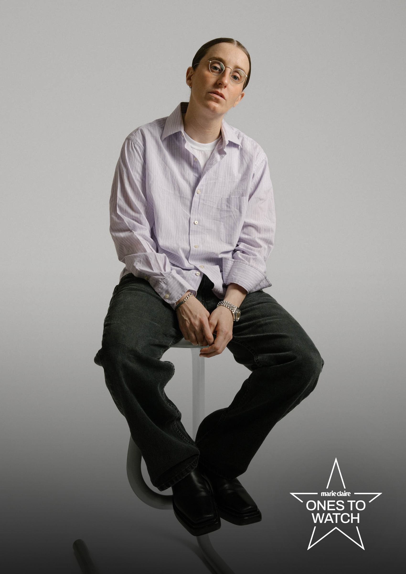 comedian robby hoffman poses in a purple shirt and black jeans sitting on a stool