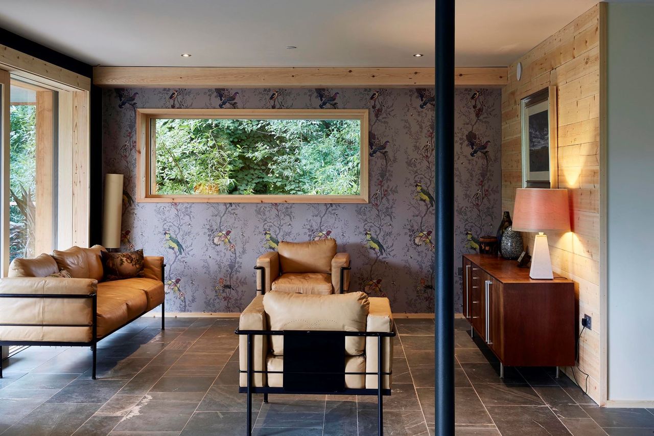 The living room has wooden walls and leather sofas and a black pole running in the middle of the room