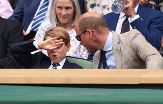 Prince George covering his eyes at Wimbledon as his dad Prince William leans in wearing sunglasses