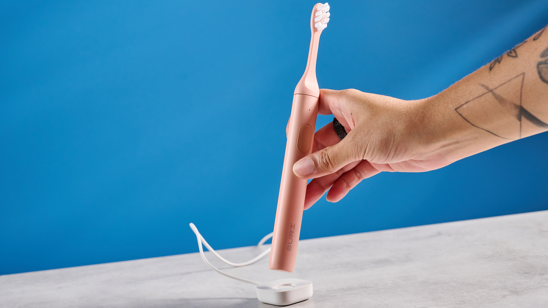 the Suri 2.0 toothbrush in sunset bloom pink colorway with a plant-based head and aluminum body, pictured with its uv cleaning travel case and the suri toothpaste