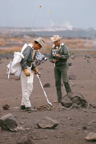Two crewmembers of NASA's Apollo 13 lunar landing mission practice using tools from the Apollo Lunar Hand Tools and a gnomon. Astronauts Jim Lovell (left) and Fred Haise are pictured carrying cameras and communications equipment during the simulation.