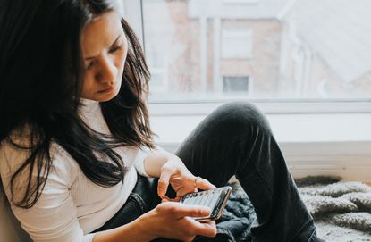 Woman sitting by a window looking at her smart phone