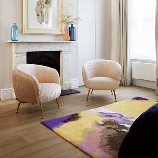 Neutral formal living room with two pale pink armchairs and brightly coloured rug