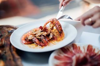 A plate of Spanish-style grilled shrimps, cooked with lemon juice, olive oil and sea salt. With Jamon Iberico in the background