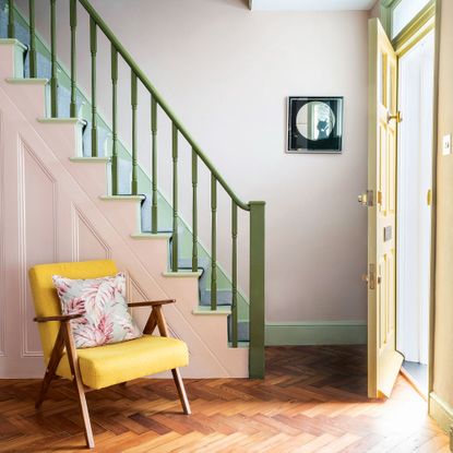 Green staircase with white and pink walls with yellow chair at foot of stairs