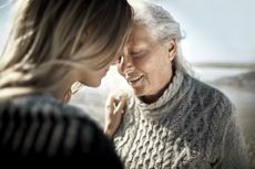 an older mother relaxes close to her daughter on a beach. The mood is calm and loving.