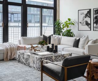 Small couch tucked into cozy living room apartment space with grey tones, house plants, and marble finish coffee table