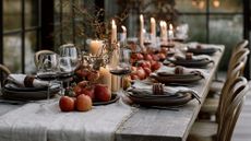 Harvest decor-inspired fall table styled with apples, softly glowing taper candles, a beige linen table runner, and textured wooden napkin rings.
