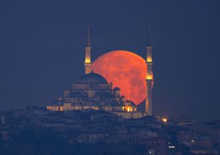the full moon appears red as it rises behind a temple