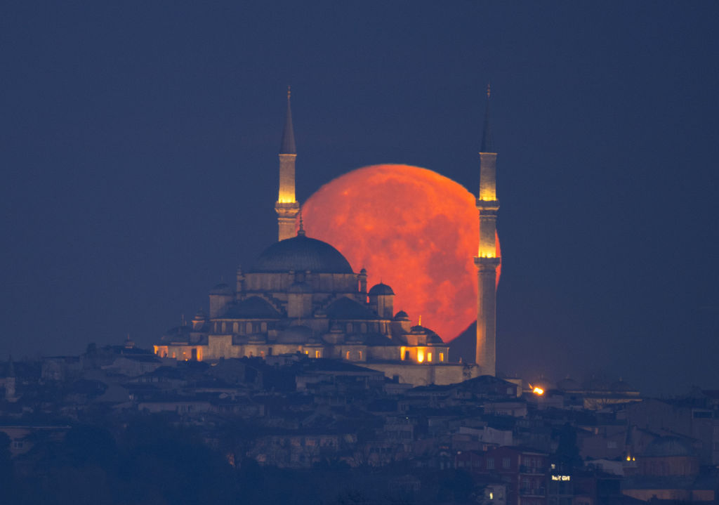 The full moon appears red as it rises behind the temple