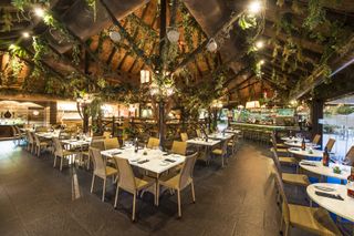 Safari restaurant at Wyndham Residences, Costa Del Sol. The photograph shows the pitched straw roof that is decorated with faux foliage, plus rows of white tables and wicker chairs
