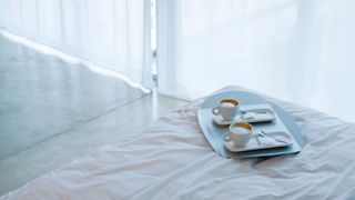 Two cups of coffee on a white bed with veiled curtains in the background