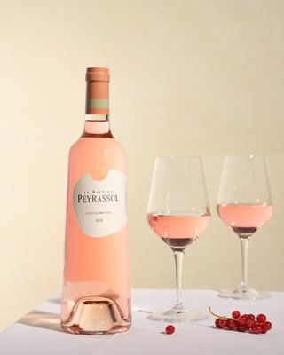 A bottle of La Bastide Peyrassol, partially filled wine glasses and fruit against a light pink background