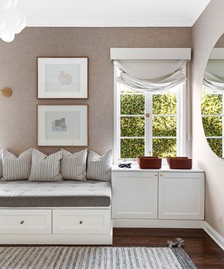 Mirror adjacent to window overlooking garden in corner of bedroom with white fabric ottoman