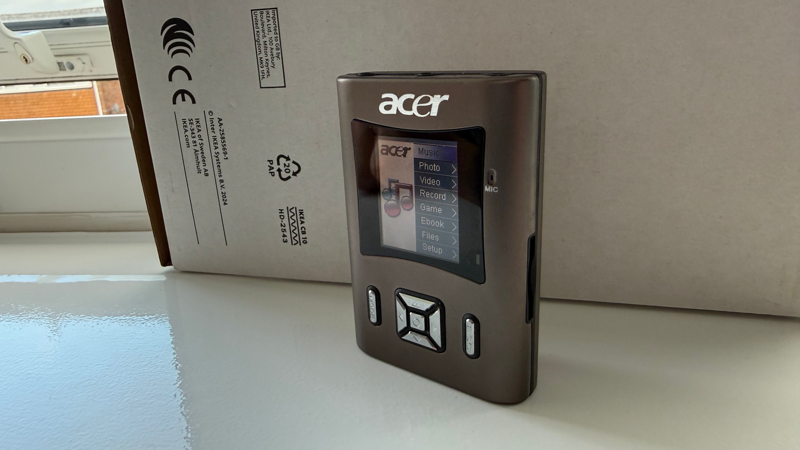 An Acer MP340 standing at a slight angle in front of its box on a windowsill.