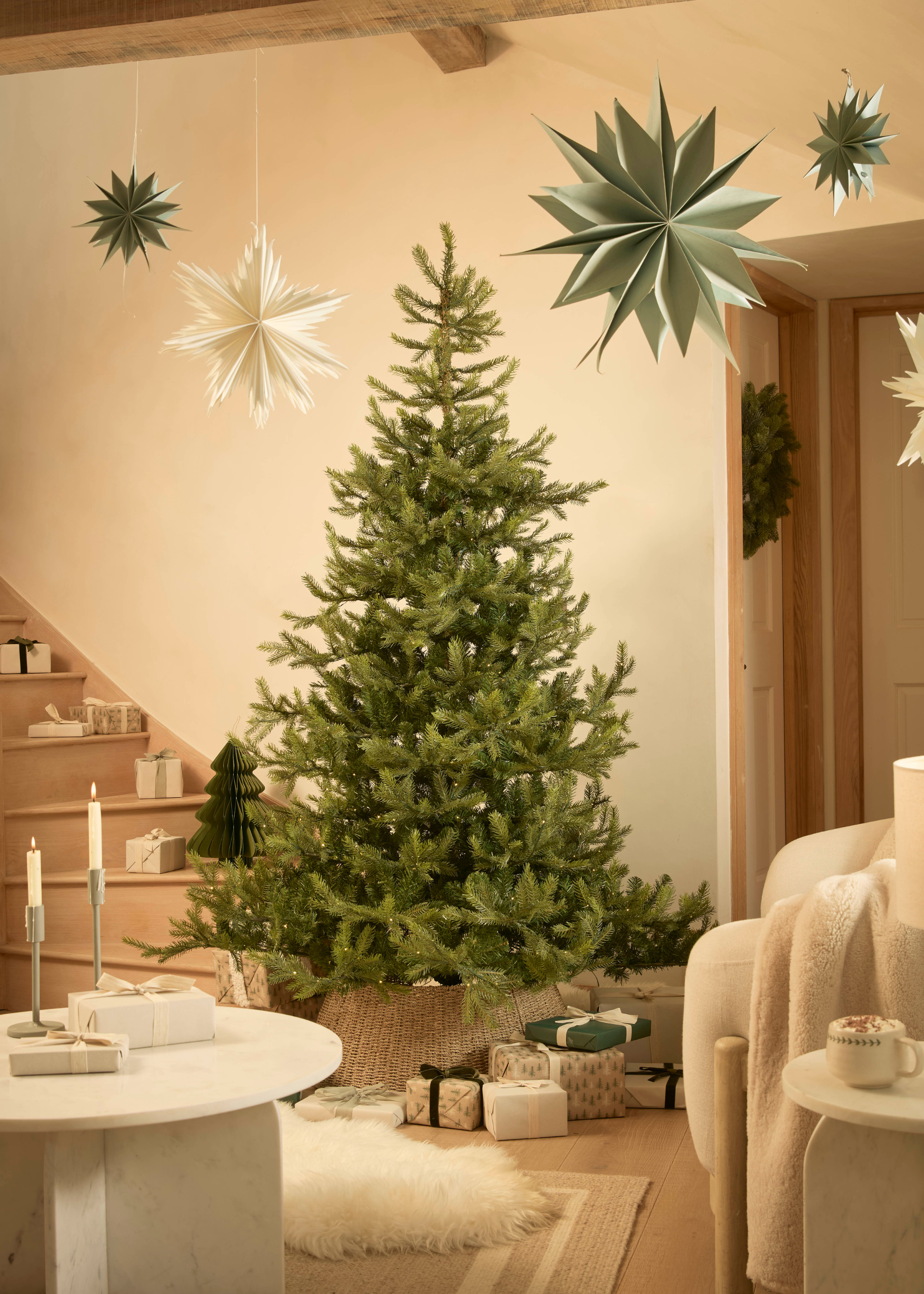 A Christmas tree in a living room with hanging paper stars, a scattering of wrapped presents, and lit taper candles
