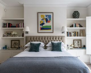 Small bedroom storage ideas built into alcoves either side of an upholstered bed with blue throw.