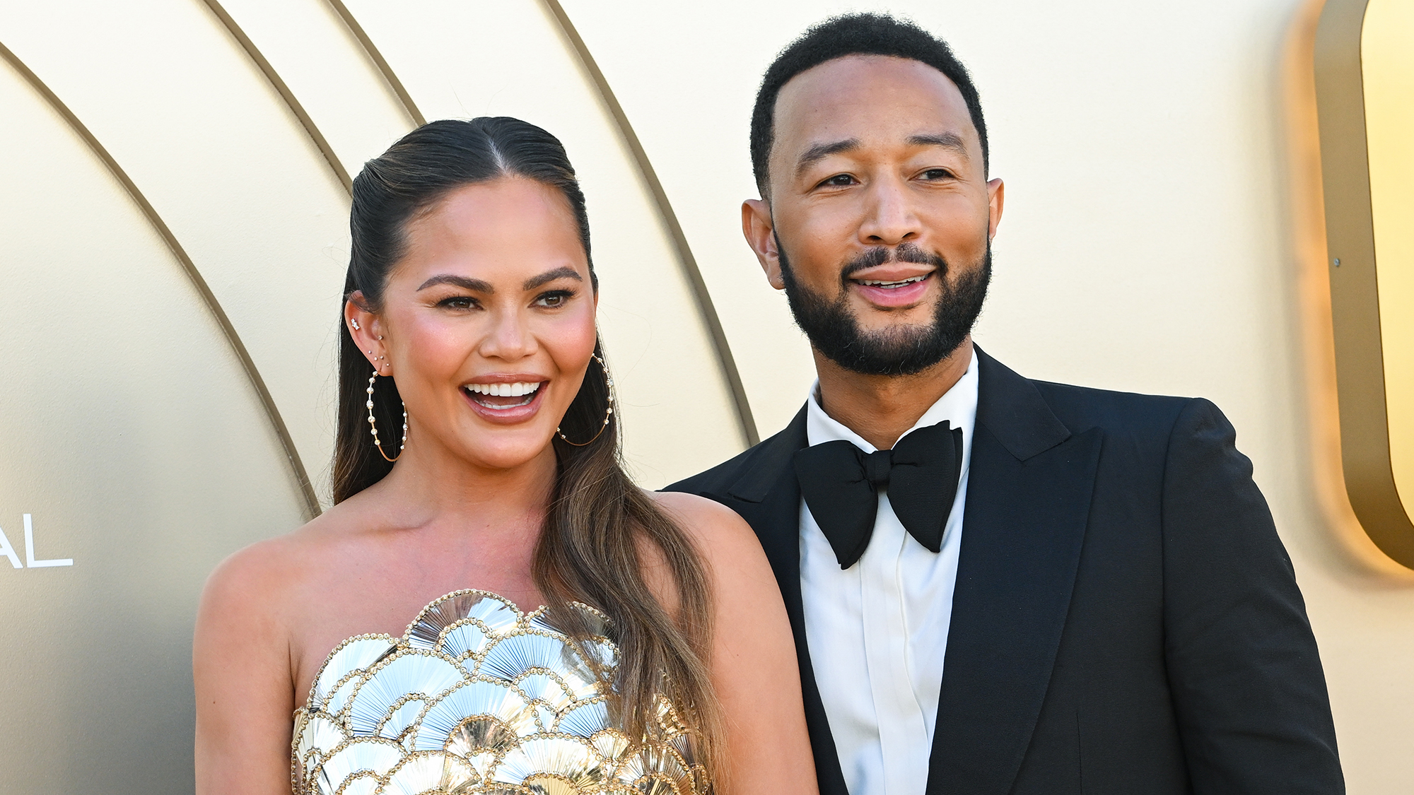 Chrissy Teigen and John Legend in formal wear in front of gold background