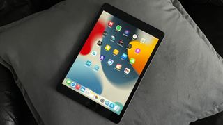 Apple iPad 10.2 (2021) i portrettmodus liggende på en grå pute.