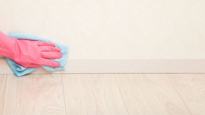 Someone wearing a pink cleaning glove wiping baseboards