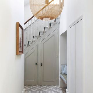 Hallway with the staircase and built in cupboards, large woven lampshade and grey and white tiled floor