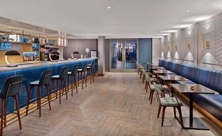 Bar area of the Le Méridien Etoile hotel, Paris, France with wooden floor, blue leather bench seat and bar stools and gold lights