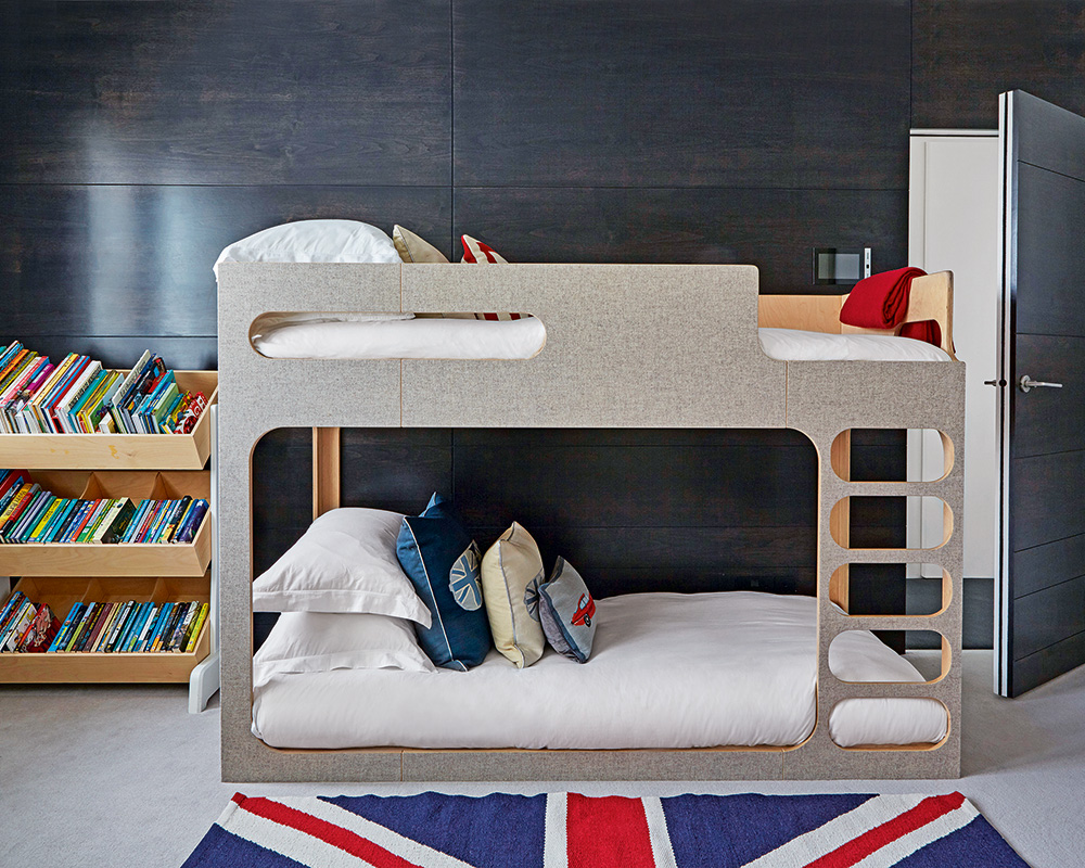 A gray panelled wall with bunk bed, bookshelves and Union Jack rug.