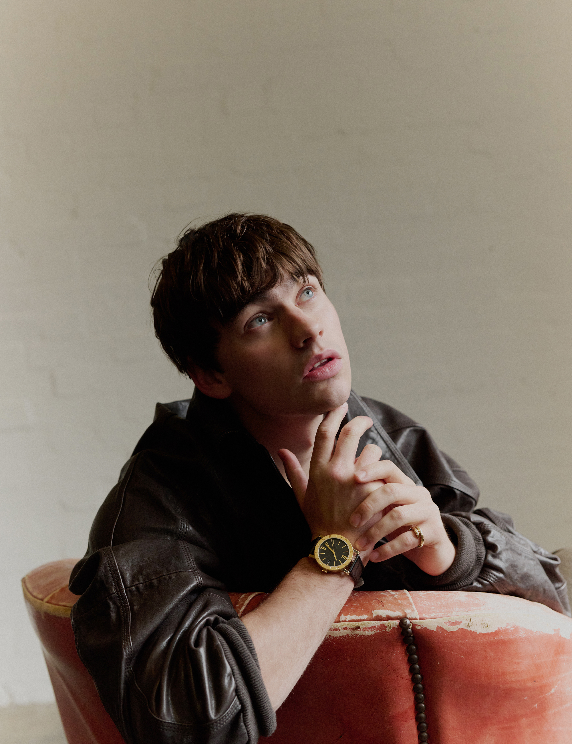 Spike Fearn looks up at the ceiling while sitting in an old worn orange leather chair. He is wearing a dark brown leather jacket and Bulgari watch.