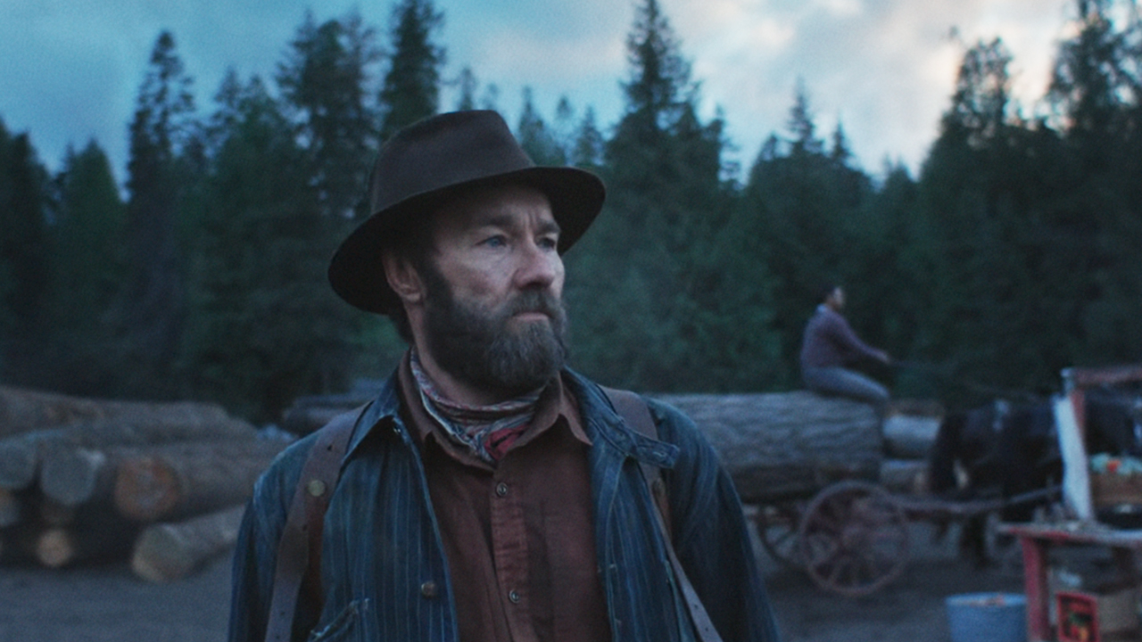 Joel Edgerton as Robert in Train Dreams, walking in a logging camp