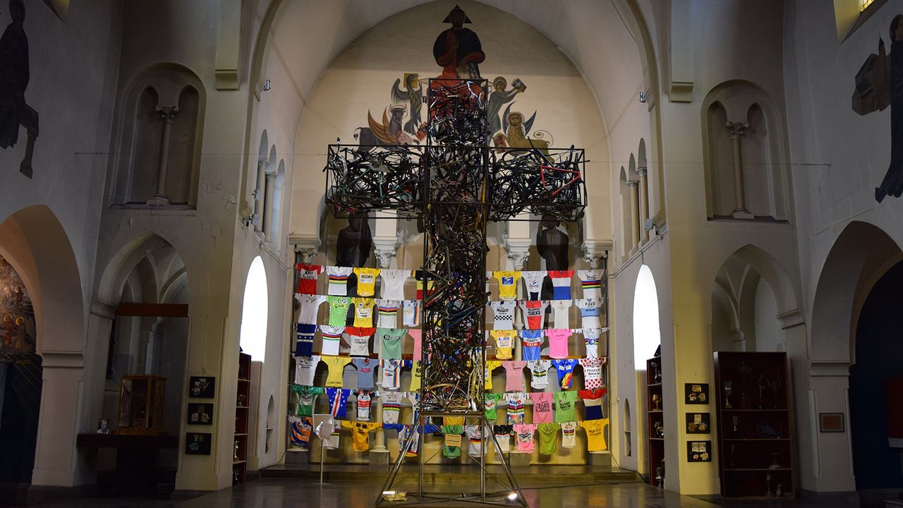 An 'iron cross' consisting of hundreds of welded bicycles and parts sits at the head of the church with the wall of jerseys as a backdrop