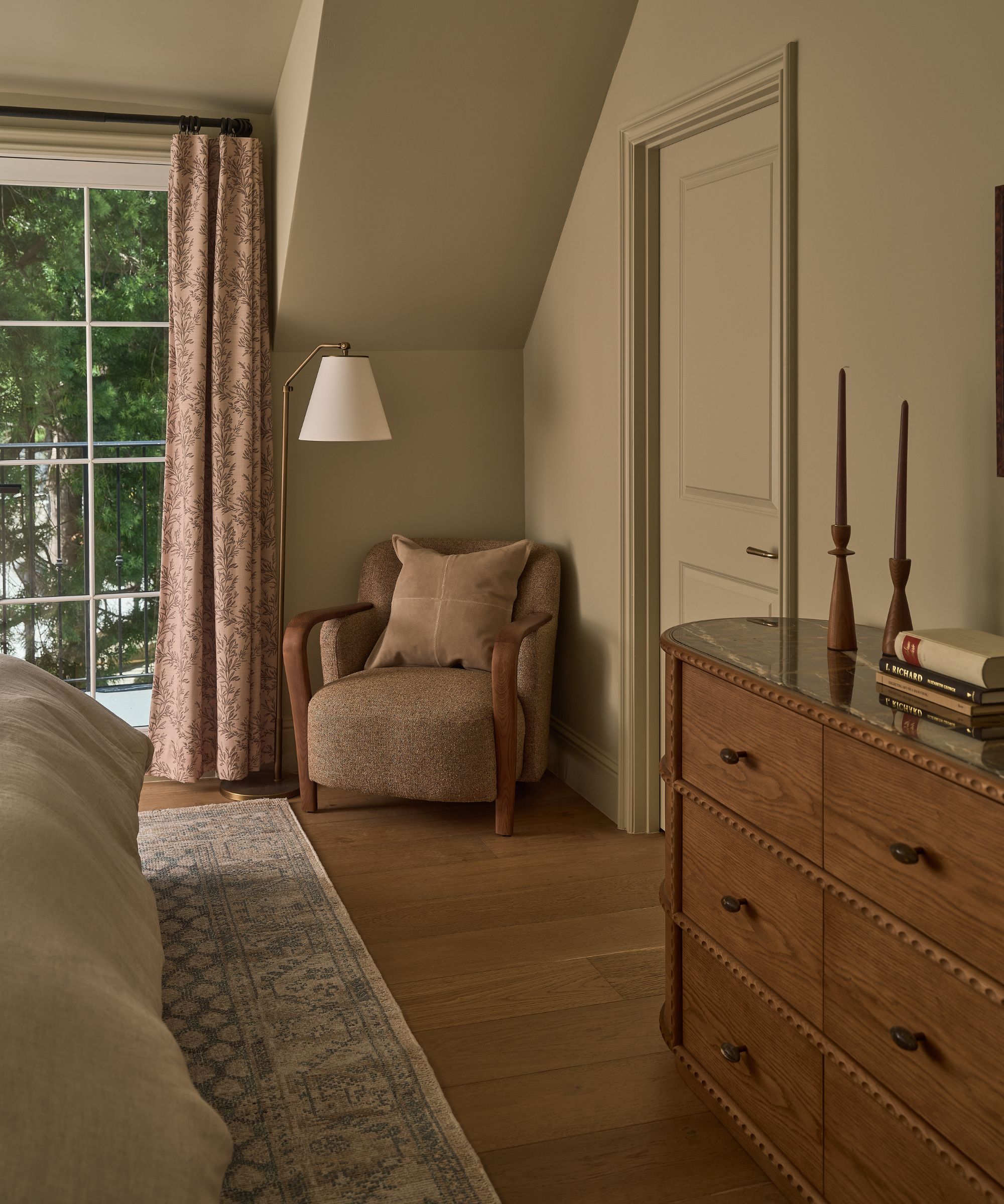 a warm neutral guest bedroom with french doors, floral drapes, a vintage style rug and a marble topped dresser