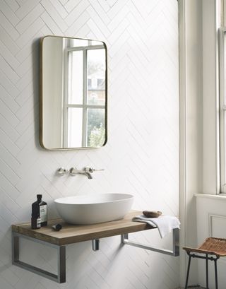 White herringbone tiles with rounded corner mirror and freestanding vanity sink.