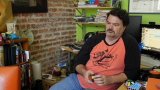 Tim Schafer sits at his desk, playing with a Rubik's cube in a Double Fine documentary video.