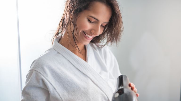 Woman in dressing gown with hairdryer in her hand