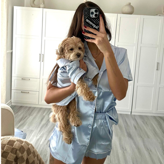 Woman taking a selfie in the mirror, holding her dog and wearing matching blue satin pajamas