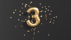 A gold balloon shaped like the number three against a black background with gold confetti.
