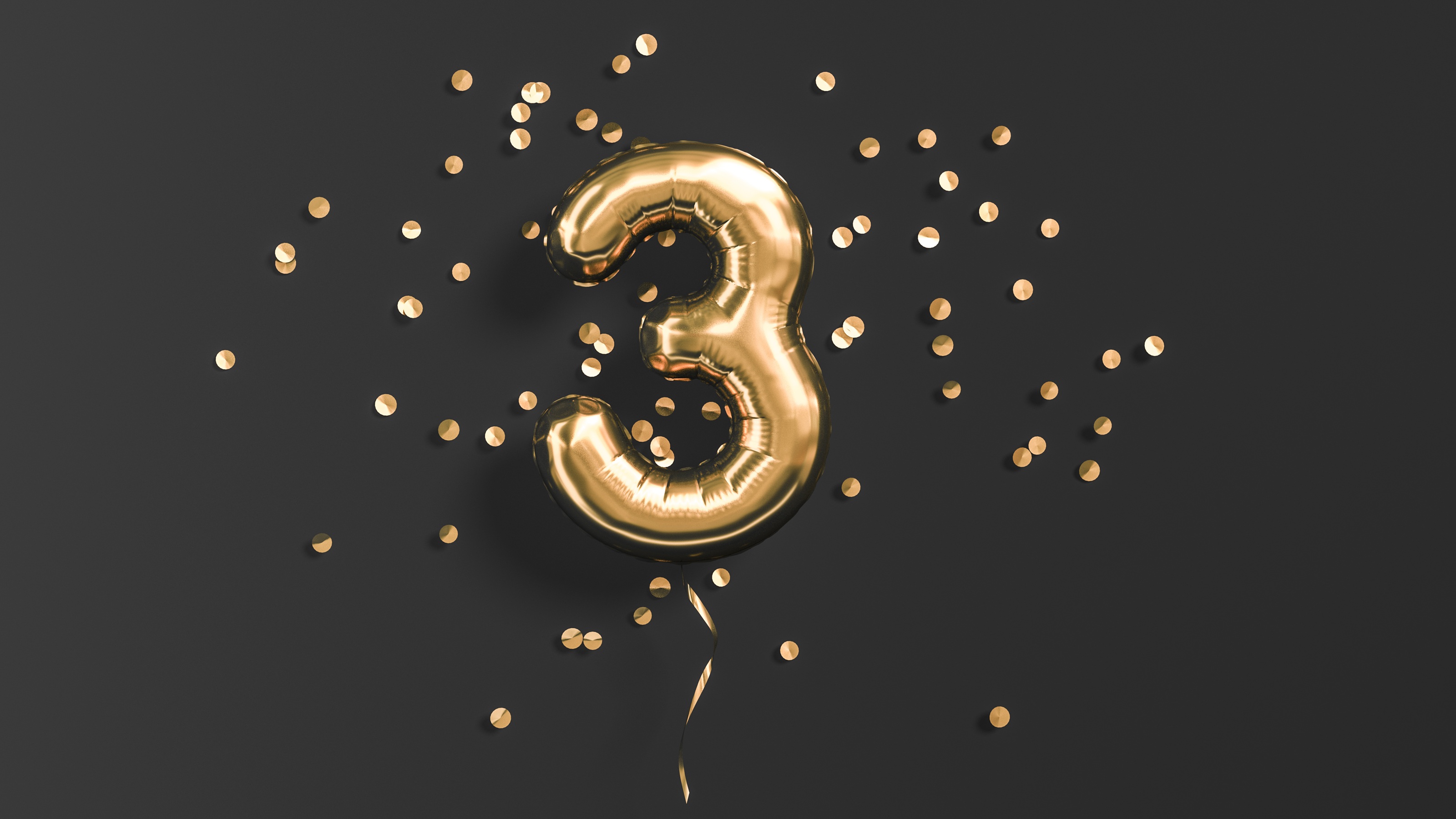 A gold balloon shaped like the number three against a black background with gold confetti.