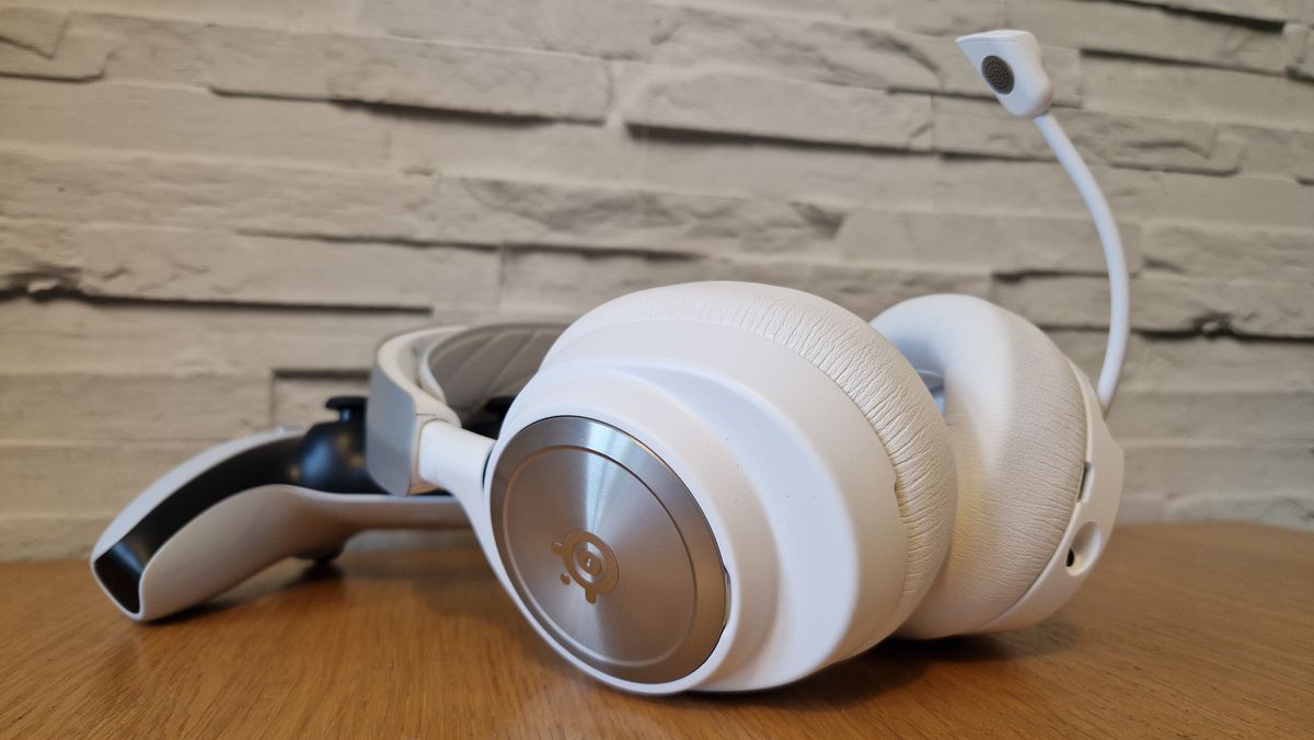 The SteelSeries Arctis Nova Pro Wireless white edition on a wooden surface with a white brick background