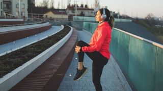 Woman stretching while out on a run, wearing over ear headphones